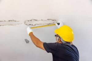 A man wearing a yellow safety helmet measures the ceiling, highlighting expert roofing services in progress.