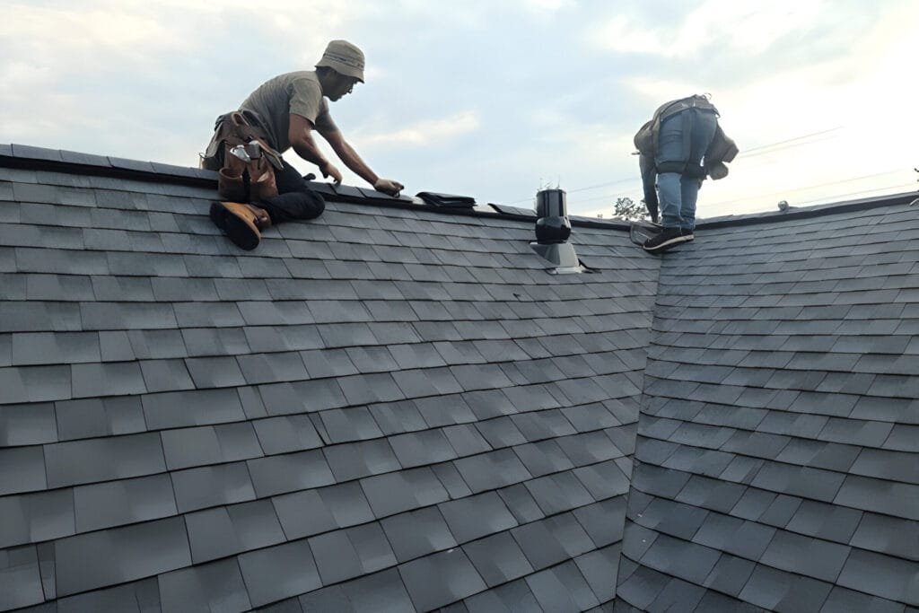 Workers engaged in roofing work, installing black shingles on a residential roof.