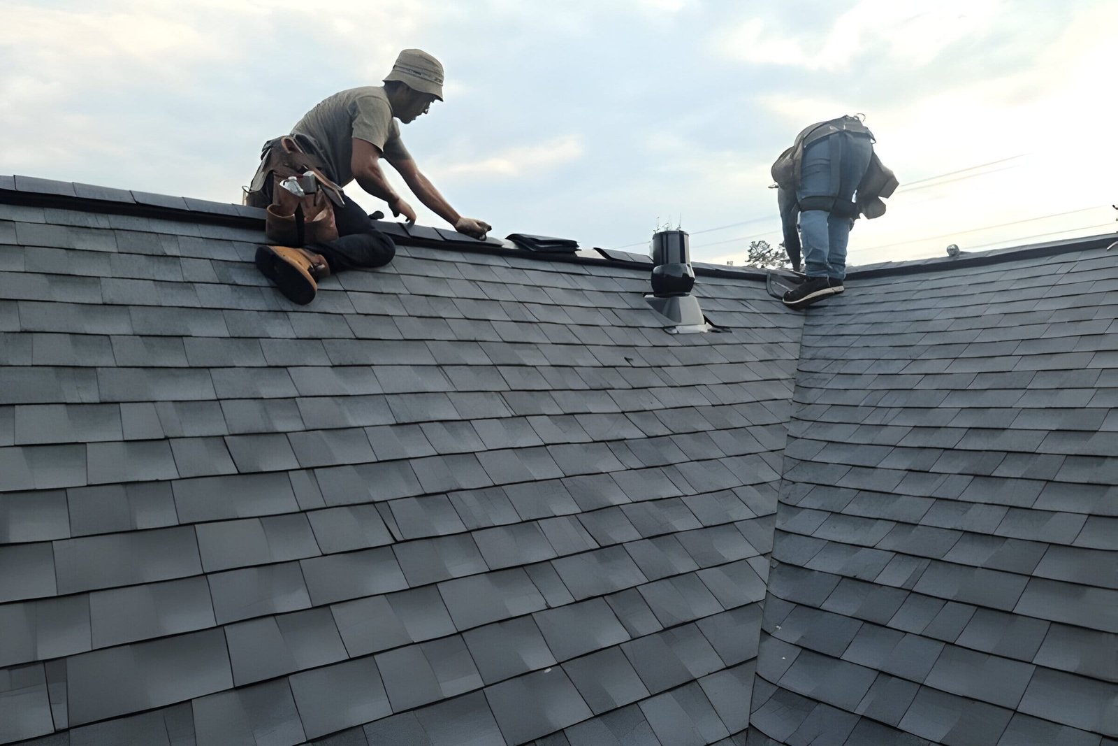 Workers engaged in roofing work, installing black shingles on a residential roof.